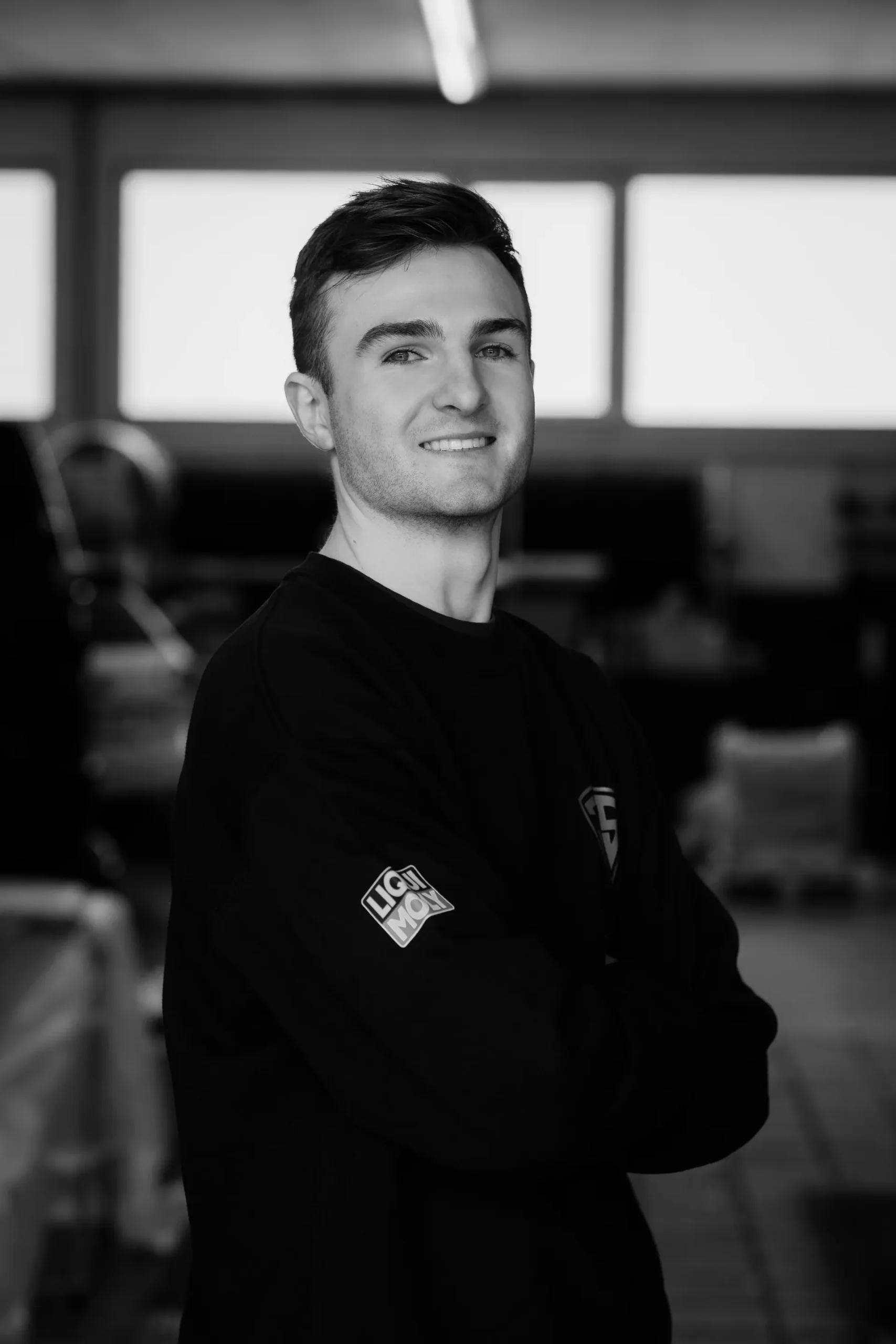 Porträt eines jungen, lächelnden Mitarbeiters in dunkler Arbeitskleidung.