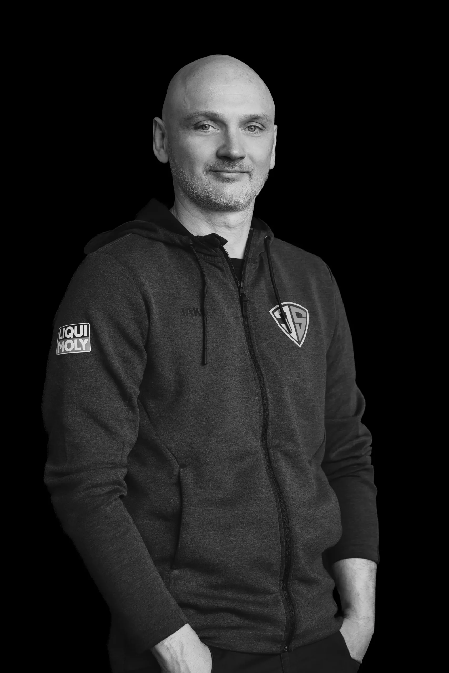 Porträt eines Mitarbeiters im dunklen Kapuzenpullover mit Firmenlogo.