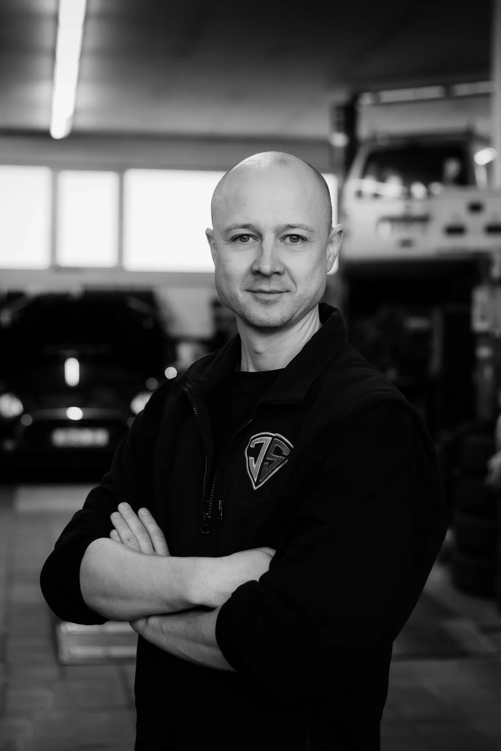 Porträt eines Mitarbeiters mit verschränkten Armen vor Autos in der Werkstatt.