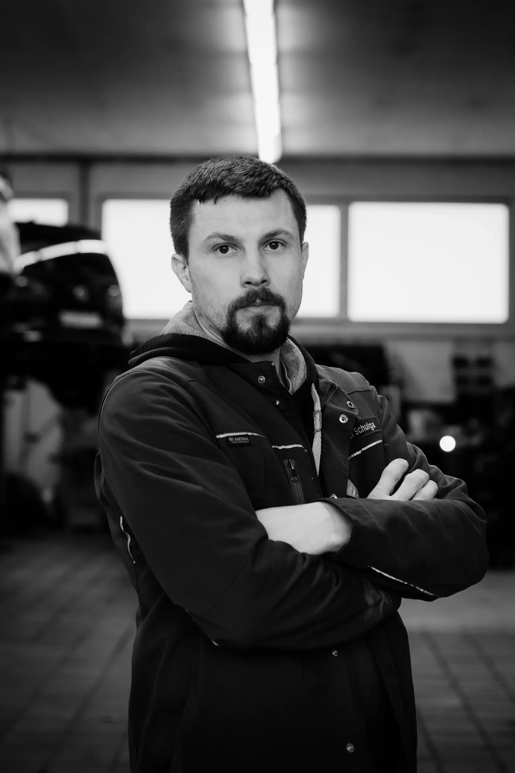 Porträt eines Mitarbeiters mit verschränkten Armen in der Werkstatt.